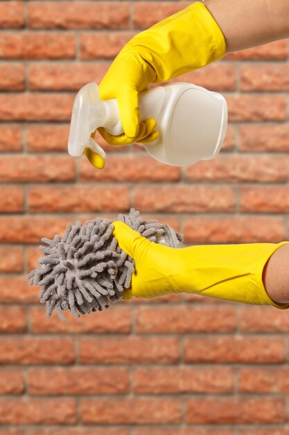 Manos de mujer en guantes protectores con botella de líquido de lavado