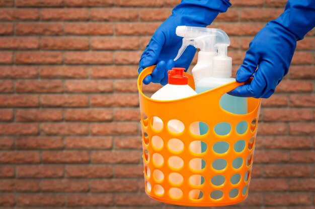 Manos de mujer en guantes protectores con botellas de limpiacristales en canasta naranja