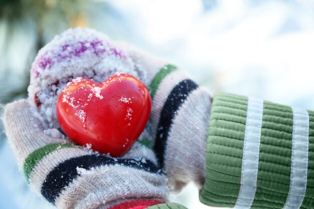 Manos de mujer en guantes de punto con corazón rojo sobre fondo de invierno