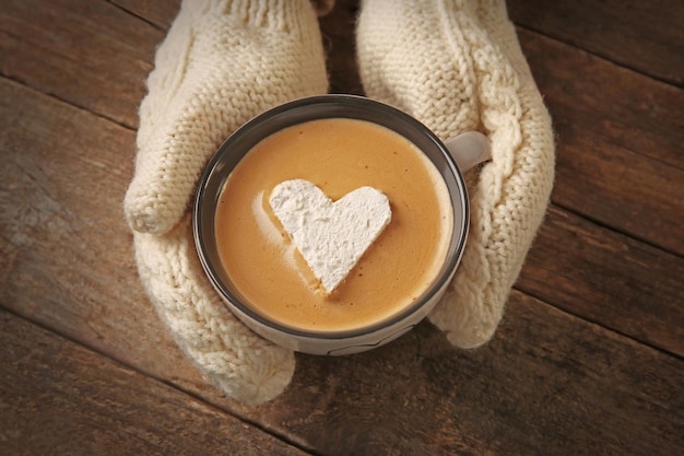 Manos de mujer en guantes sosteniendo una taza de café