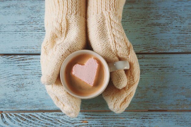 Manos de mujer en guantes sosteniendo una taza de café