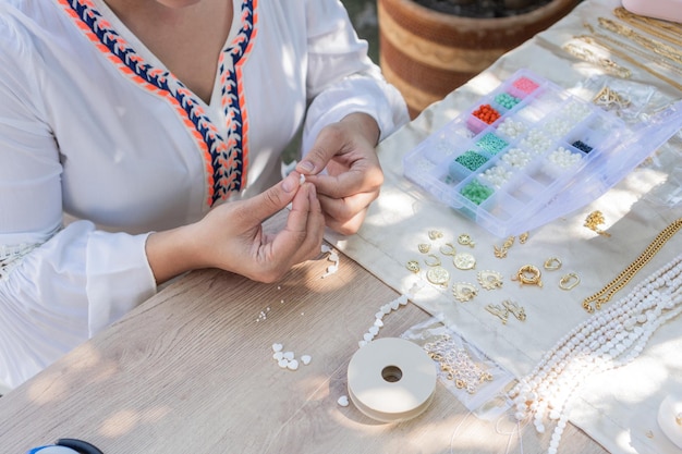 Las manos de una mujer haciendo collares en su taller