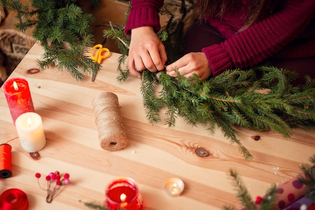 Manos de una mujer haciendo corona de Navidad de ramas de abeto natural