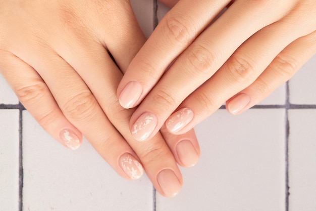 Manos de mujer hermosa con diseño de uñas nude sobre fondo blanco manicura pedicura salón de belleza conc