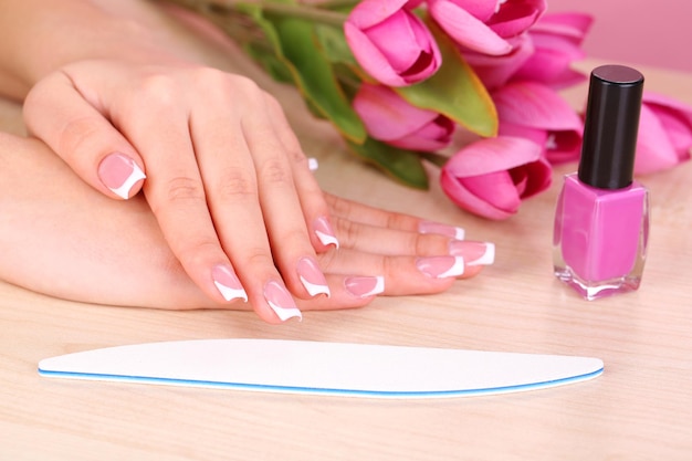 Manos de mujer hermosa con manicura francesa y flores sobre fondo de madera