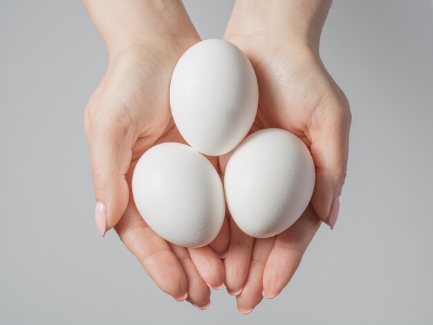 Manos de mujer con huevos blancos aislados en gris