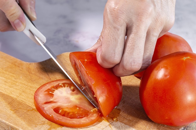 Manos de mujer irreconocible cortando rodajas de tomate fresco sobre una tabla de madera