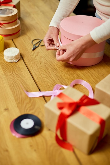 Manos de mujer irreconocible envolviendo con cinta un regalo rosa