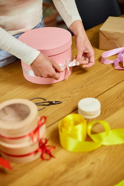 Manos de mujer irreconocible envolviendo con cinta un regalo rosa