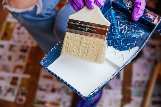 Foto manos de mujer irreconocibles con guantes morados tomando pintura con un pincel en una bandeja reformas