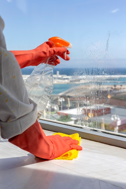 Manos de mujer irreconocibles con guantes protectores limpiando la casa