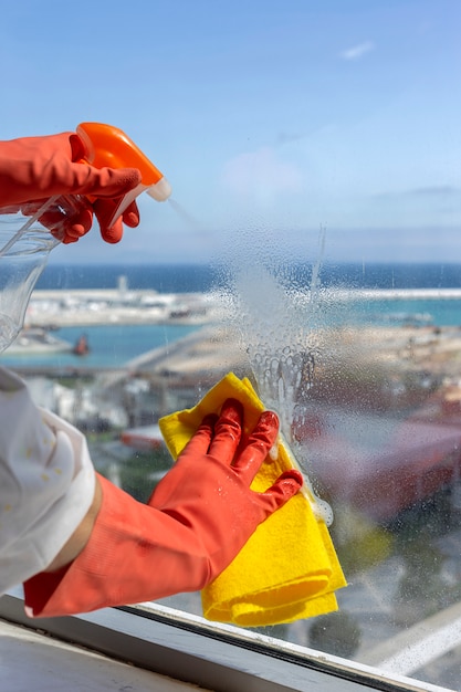 Manos de mujer irreconocibles con guantes protectores limpiando la casa