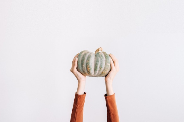 Manos de mujer irreconocibles sosteniendo calabaza sobre fondo blanco con espacio de copia