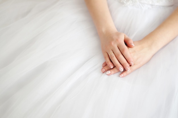 Manos de una mujer joven con un anillo de compromiso en el fondo de un vestido de novia