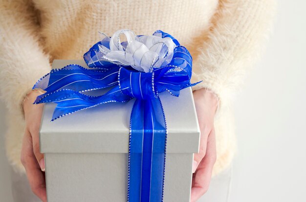 Manos de mujer joven con caja de regalo de plata con cinta azul y blanca