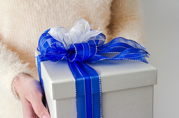 Manos de mujer joven con caja de regalo de plata con cinta azul y blanca