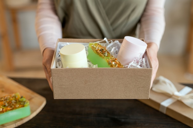 Manos de mujer joven empacar barras de jabón natural hecho a mano fresco en caja de regalo de cartón mientras prepara regalos para sus amigos antes de las vacaciones