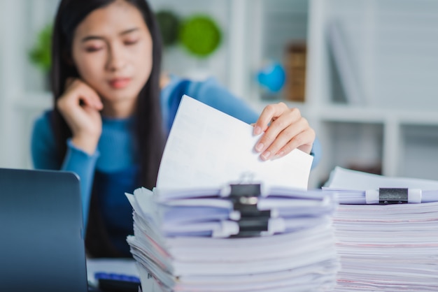 Las manos de la mujer joven del empleado que comprueban la pila de archivos de papel para buscar documentos inacabados después de terminar el trabajo duro ocupado.