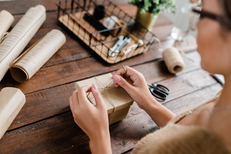 Foto manos de mujer joven haciendo nudo de hilos en la parte superior de la caja de regalo
