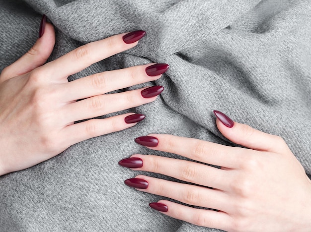 Manos de una mujer joven con manicura de color rojo oscuro en las uñas