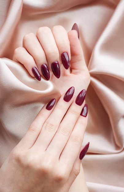 Manos de una mujer joven con manicura de color rojo oscuro en las uñas