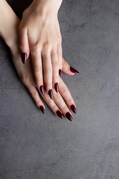 Manos de una mujer joven con manicura de color rojo oscuro en las uñas