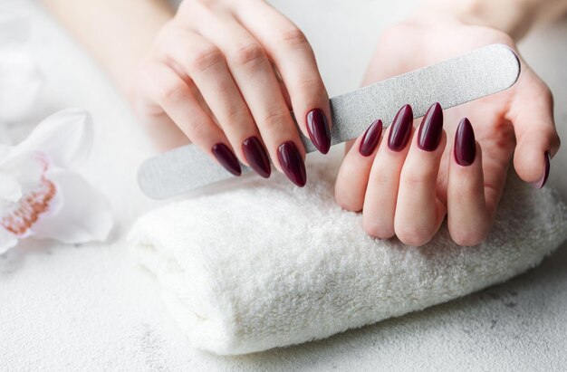 Manos de una mujer joven con manicura de color rojo oscuro en las uñas