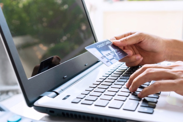 manos de mujer joven navegando en el sitio web de compras en línea mientras sostiene la tarjeta de crédito