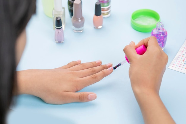 Foto manos de una mujer joven pintando sus uñas con un barniz y accesorios para uñas en la mesa