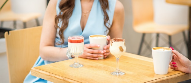 Manos de una mujer joven sosteniendo una taza de café con diferentes cócteles en la mesa del café