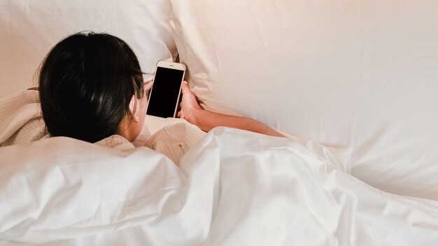 Manos de mujer joven sosteniendo el teléfono inteligente en la cama después de despertarse.