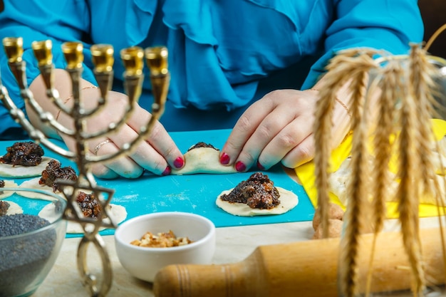 Las manos de una mujer judía con un tocado tradicional hacen galletas gomentash triangulares