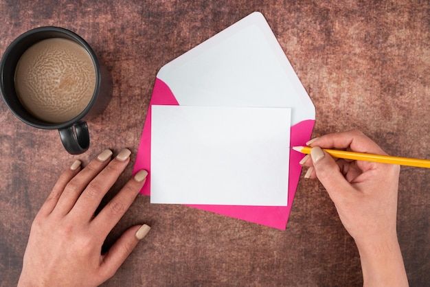 Manos de mujer con lápiz Sobre de papel en blanco y taza de café sobre fondo de madera Empresaria tomando bebida y escribiendo un mensaje crucial en una carta comercial