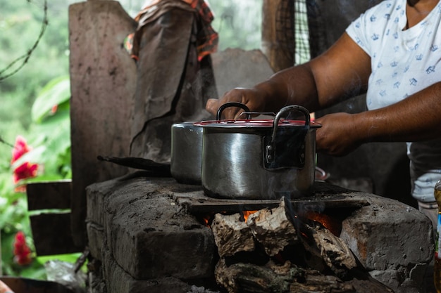 manos de una mujer latina, una campesina de piel marrón que sostiene una olla de hierro encima de una estufa tradicional