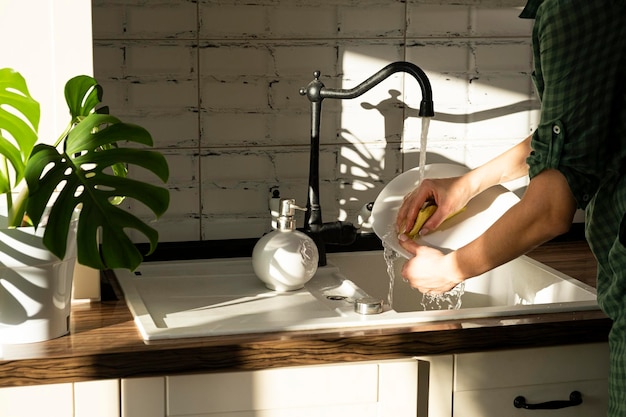 las manos de una mujer lavan los platos en casa los platos bajo un arroyo de agua en la rutina doméstica de la luz del sol