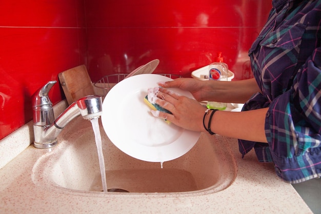 Manos de mujer lavando la placa blanca en el fregadero de la cocina