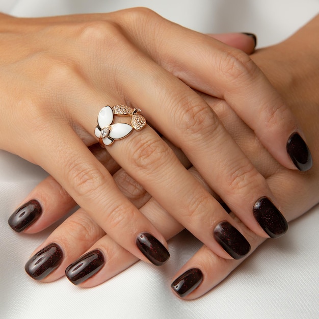 Las manos de una mujer con una manicura de color rojo oscuro y un anillo en la mano izquierda.