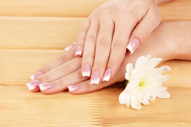 Manos de mujer con manicura francesa y flor sobre fondo de madera