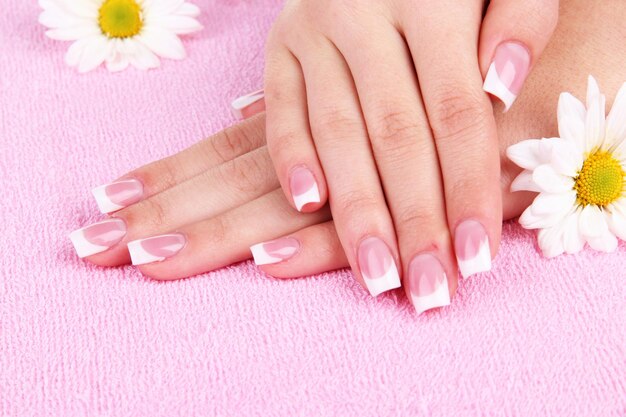 Manos de mujer con manicura francesa y flores en toalla rosa