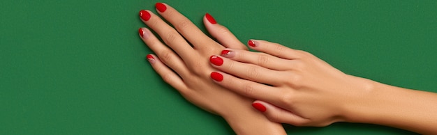 Manos de mujer con manicura roja de Navidad de moda sobre fondo verde