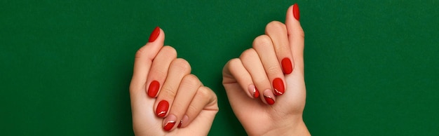 Manos de mujer con manicura roja de Navidad de moda sobre fondo verde