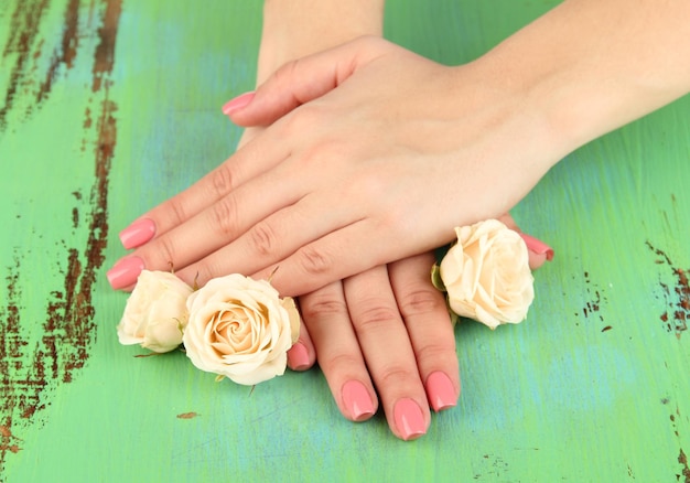 Foto manos de mujer con manicura rosa y flores en fondo de color