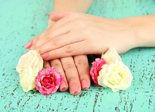 Manos de mujer con manicura rosa y flores sobre fondo de color