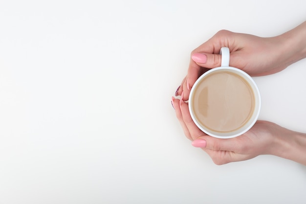 Manos de mujer con manicura rosa con taza de café,