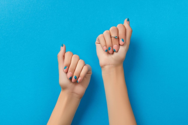 Manos de mujer con manicura de verano sobre fondo azul.