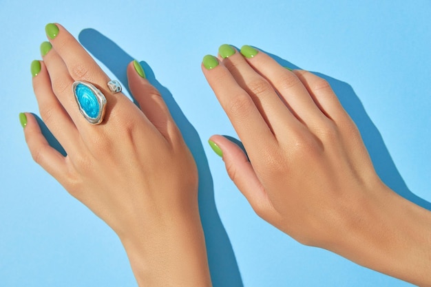 Manos de mujer con manicura verde de cerca sobre fondo azul Tratamiento de belleza spa cuidado del cuerpo Concepto de salón