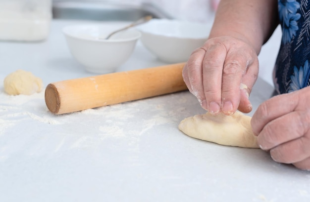 Manos de mujer mayor haciendo pasteles con relleno de manzana en una mesa de cocina blanca con rodillo de madera en el fondo Enfoque selectivo Concepto de cocina en casa Tradición comida casera