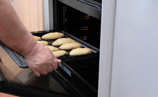 Manos de mujer mayor ponen una bandeja para hornear con pasteles crudos con relleno de manzana en el horno Enfoque selectivo Proceso de elaboración de pasteles con relleno de manzana Concepto de cocina en casa Tradición comida casera