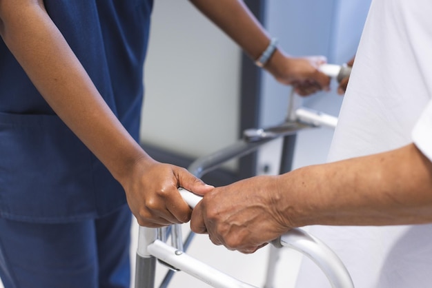 Las manos de una mujer médica afroamericana caminando con una anciana paciente con muletas en el hospital