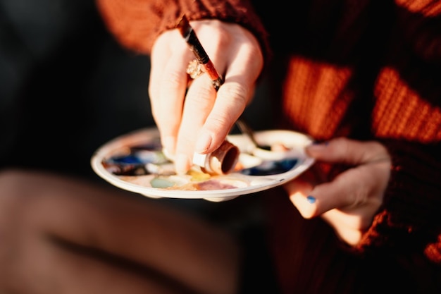 Manos de una mujer mezclando pinturas en un tablero de paleta preparándose para pintar una imagen herramientas artísticas el